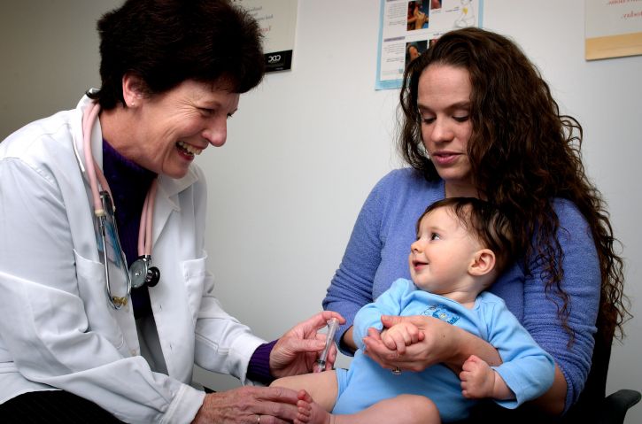 Infant being held by his mother while receiving an intramuscular vaccination in his left thigh muscle